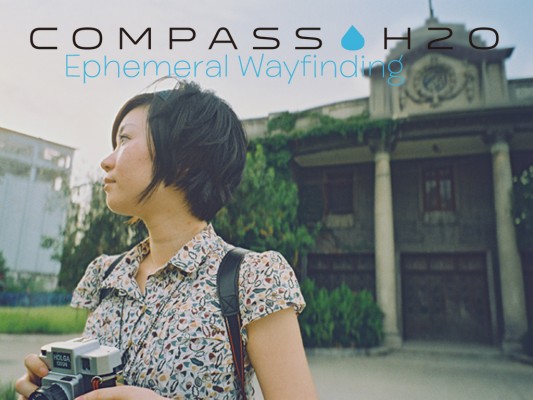 Photo of a woman in front of a vintage Shanghai building with a classical facade. The woman has a bob haircut and holds a Holga camera. Superimposed text reads: "Compass H2O: Ephemeral Wayfinding"